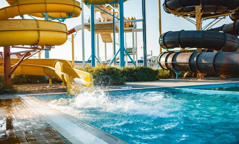 A woman descended from a large high yellow slide into a pool of clear water creating more spray