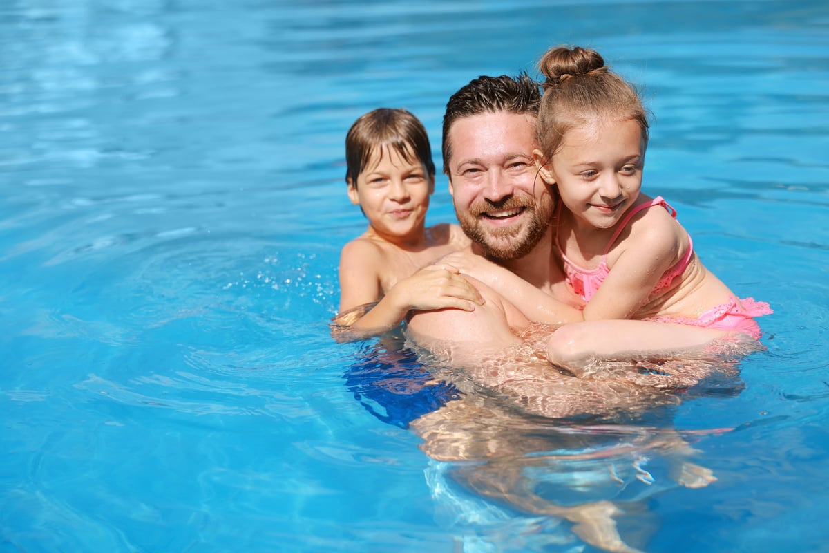 Happy father and his kids resting in swimming pool outdoors, space for text. Family vacation