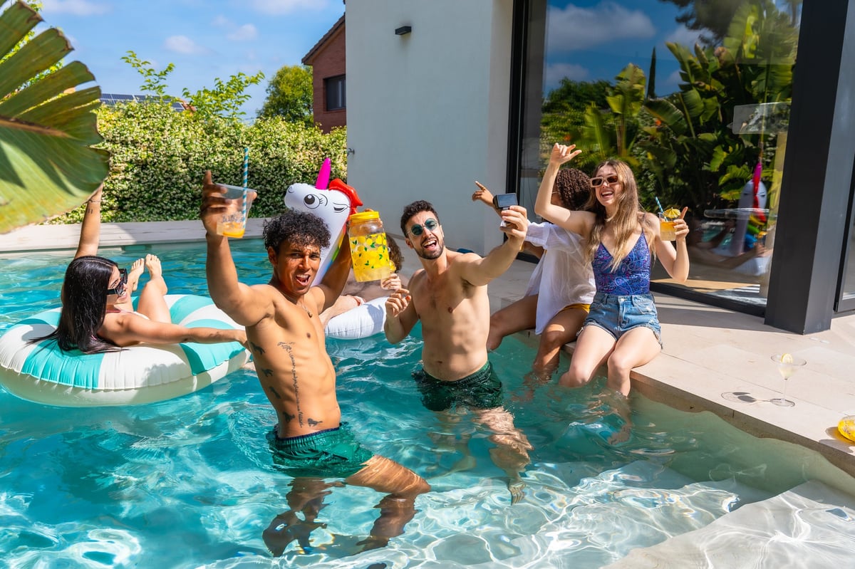 Group of diverse young adult friends enjoying a vibrant pool party cheering with drinks during a sunny outdoor gathering