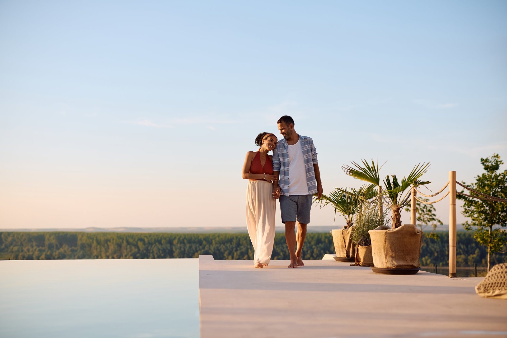Pareja feliz junto a la piscina de un resort tropical de lujo al atardecer