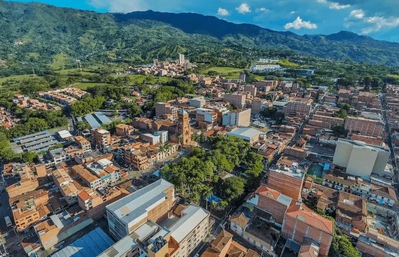 Vista aérea de un municipio colombiano con barrios densos de edificaciones coloridas rodeadas de montañas verdes bajo cielo azul