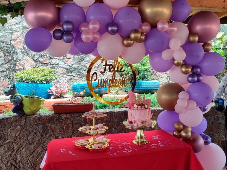 Outdoor birthday party setup with purple and gold balloon arch, red tablecloth, and Hello Sunshine banner with tiered dessert displays