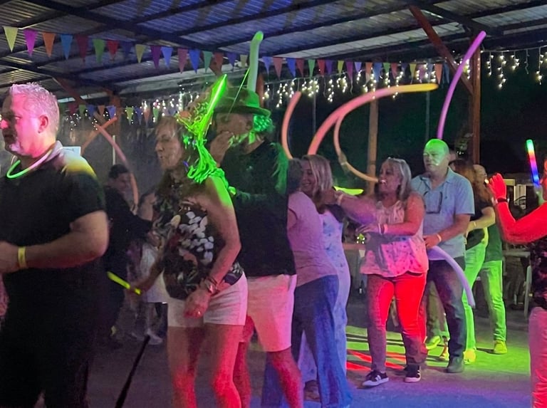 Group of people dancing at an indoor party with colorful neon lights, glow sticks, and decorated ceiling