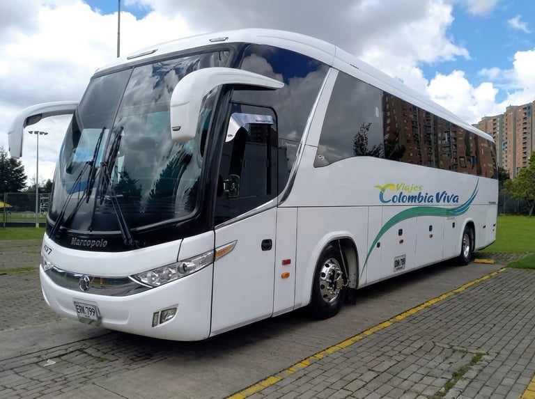 White Colombia Viva tour bus parked on street with cloudy sky and buildings in background