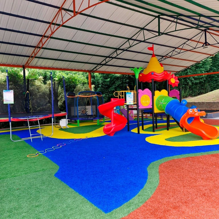 Parque infantil al aire libre a todo color con toboganes, estructuras para escalar y trampolines bajo una cubierta metálica