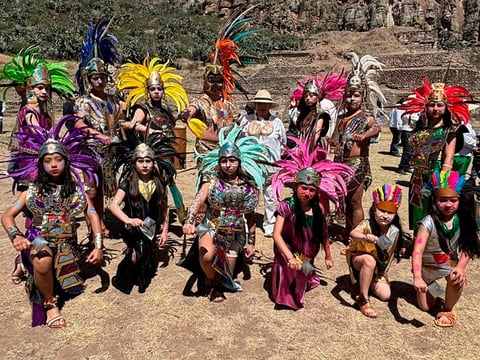 Group of festival performers in colorful feathered headdresses and elaborate costumes posing on sandy ground outdoors