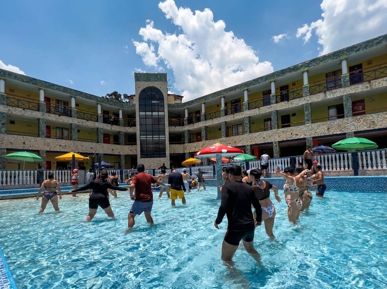 Children and adults enjoying a bright blue swimming pool at a resort hotel courtyard on a sunny day