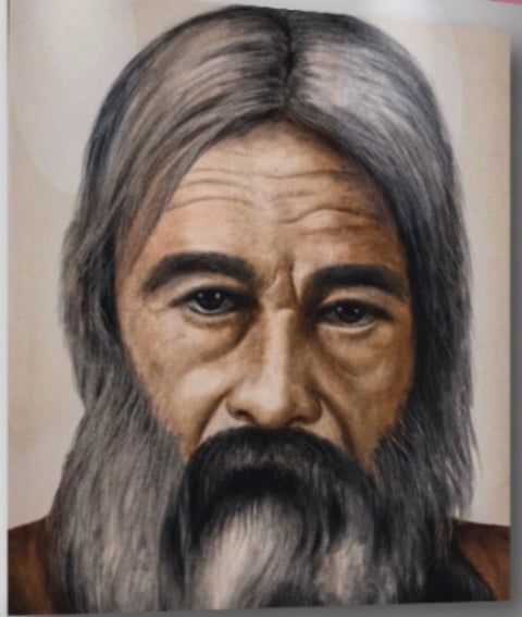 Portrait of an older man with long gray hair, full dark beard, and weathered facial features against a neutral background.