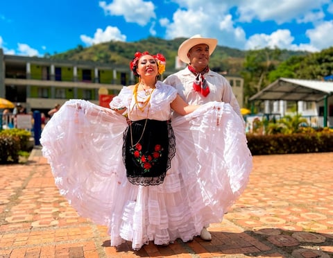 Pareja con atuendo tradicional latinoamericano con faldas rosadas con volantes bailando al aire libre en un evento comunitario