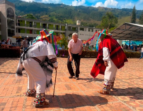Dos personas con coloridos trajes tradicionales y grandes tocados interpretan un baile cultural en un festival al aire libre en un valle montañoso