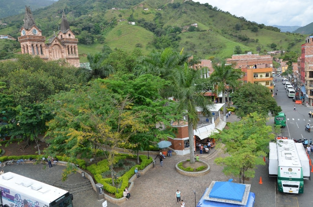 Vista aérea de Barbosa, un pueblo colombiano con iglesia colonial de ladrillo rojo, montañas verdes y calles estrechas con vehículos estacionados